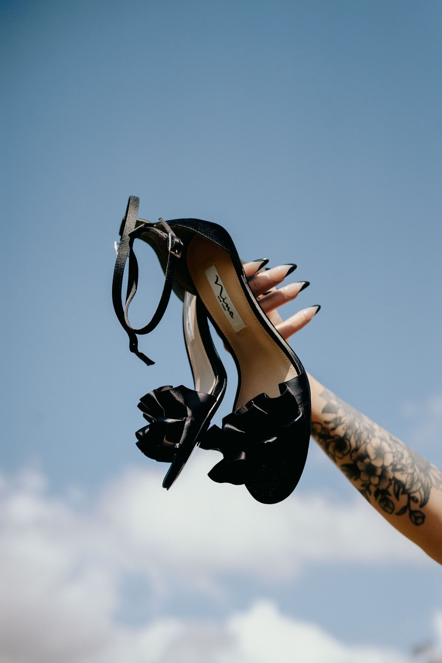 Black high heel shoe held against blue sky showing elegant design details.