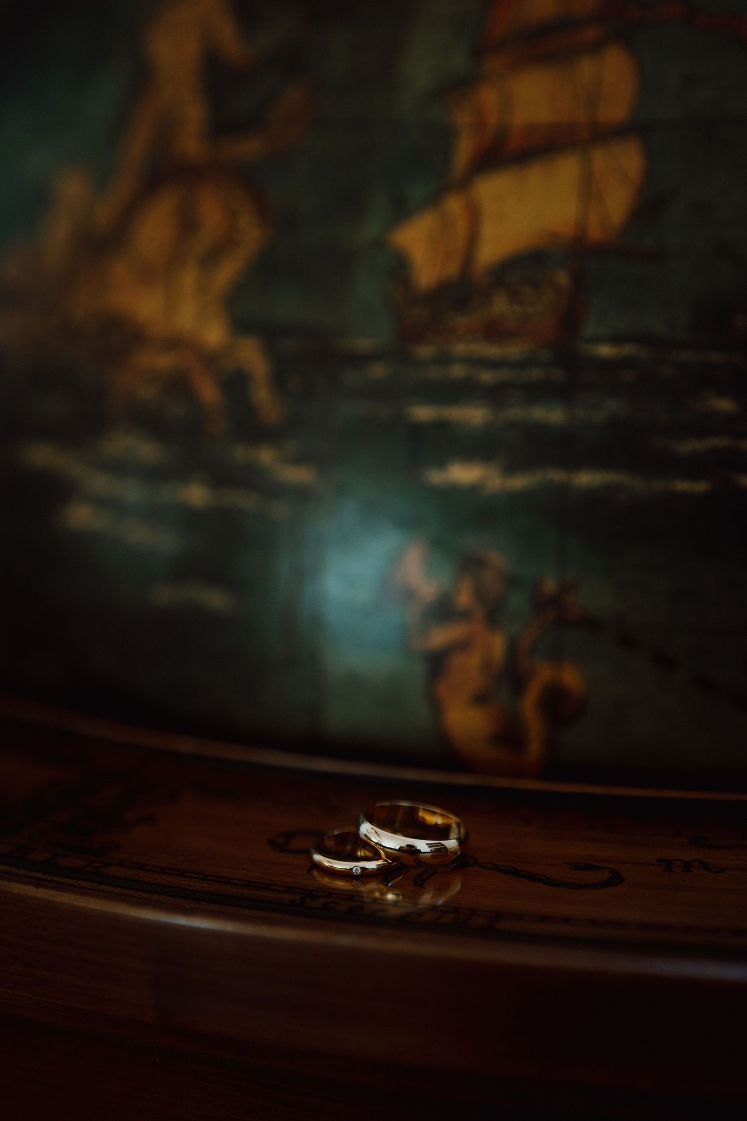 Wedding rings photographed in dramatic lighting with blurred background creating artistic composition.