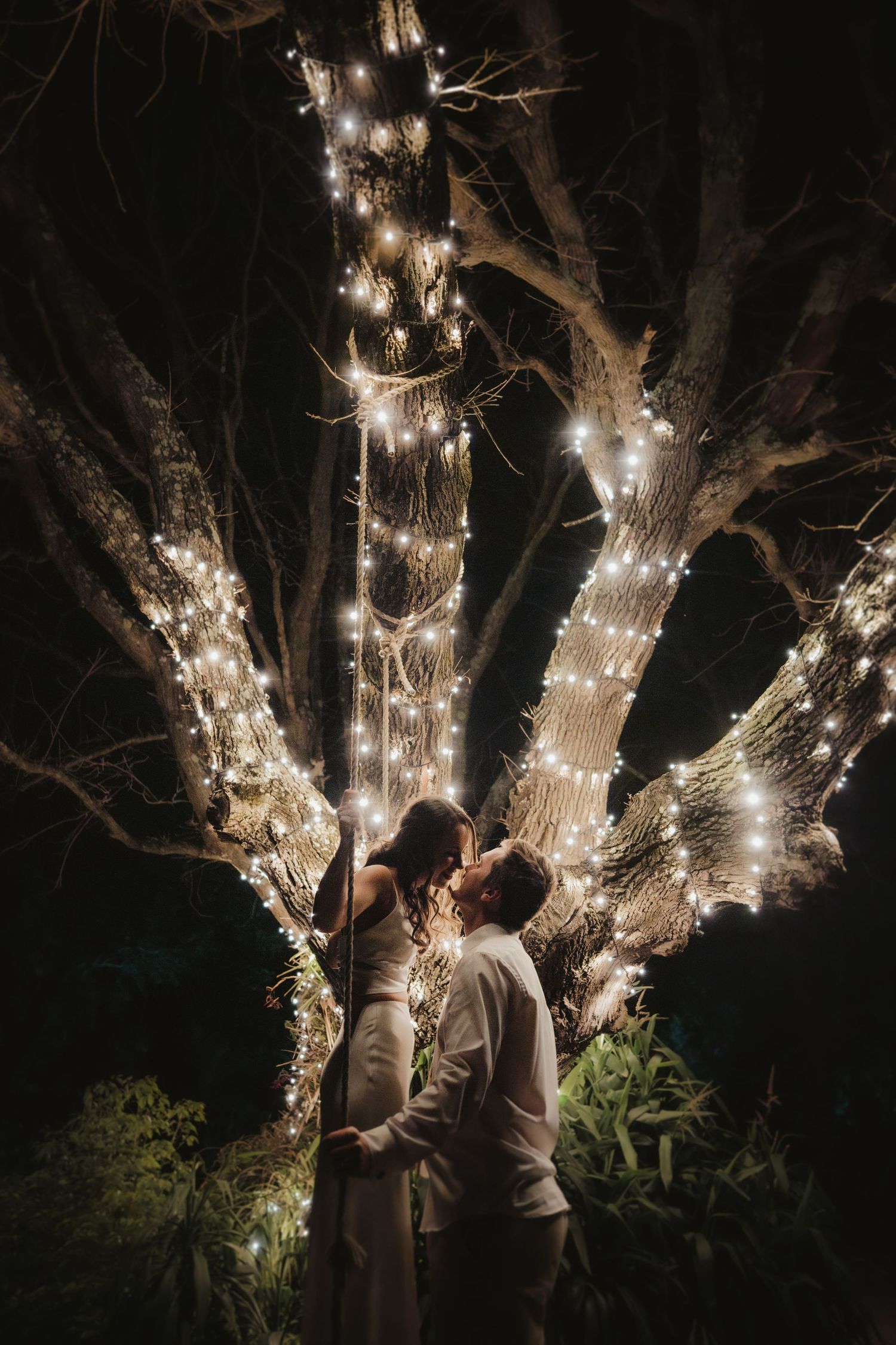 Trees decorated with twinkling string lights create a romantic nighttime garden setting.