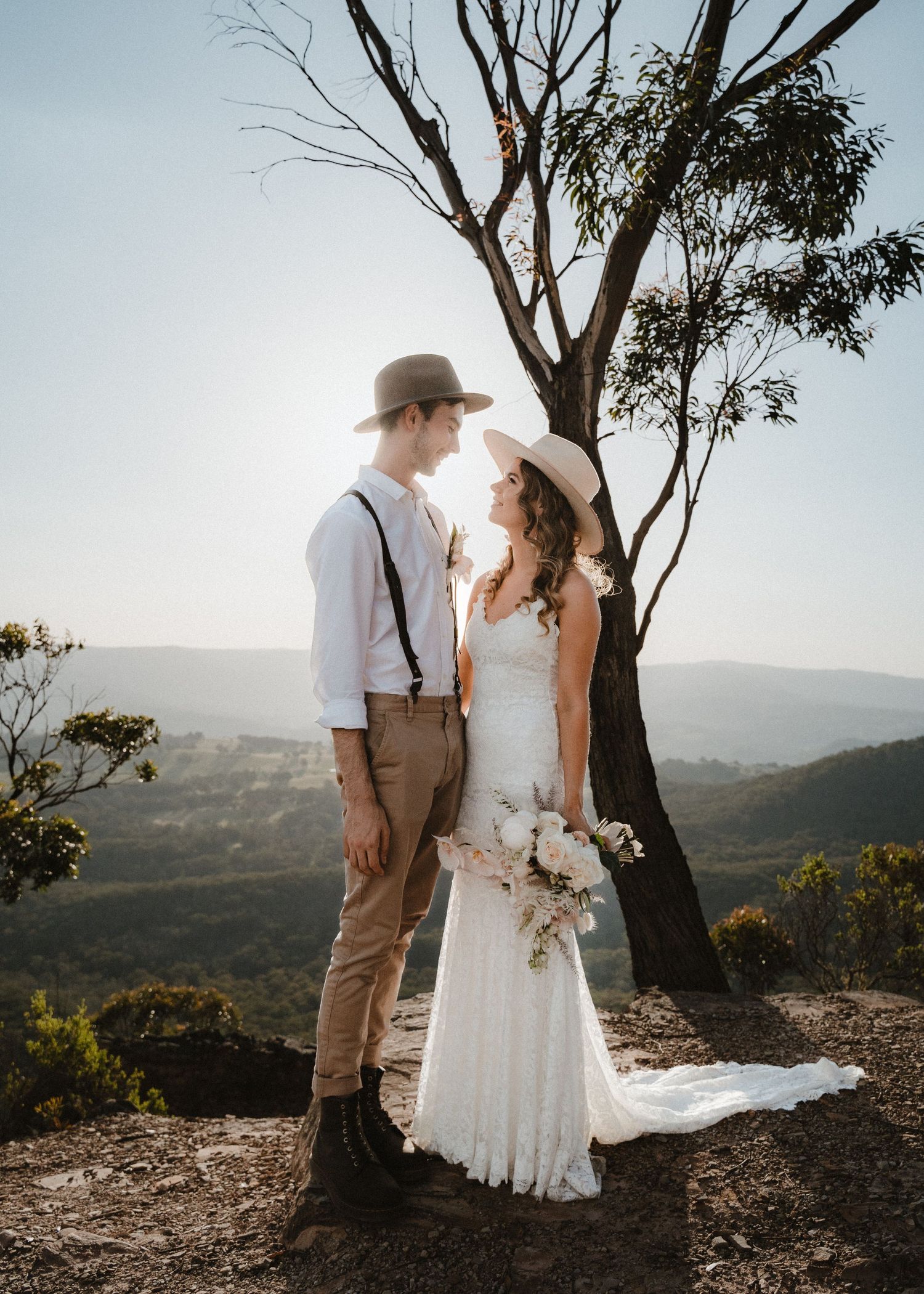 A couple poses together on a scenic mountain overlook in vintage-inspired wedding attire.