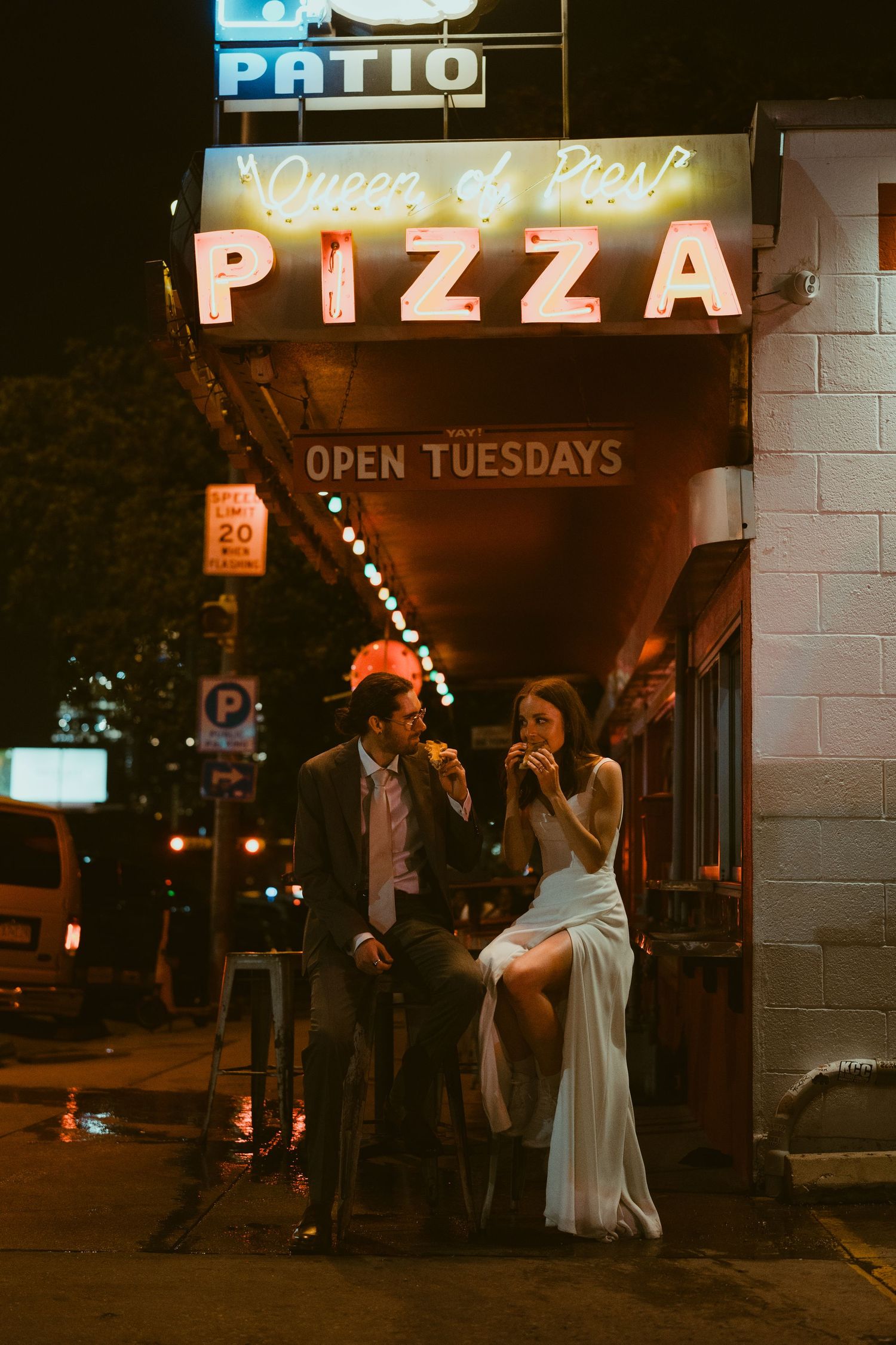 Wedding party celebrating outside a pizza shop at night with neon signs glowing in the background in Austin Texas.
