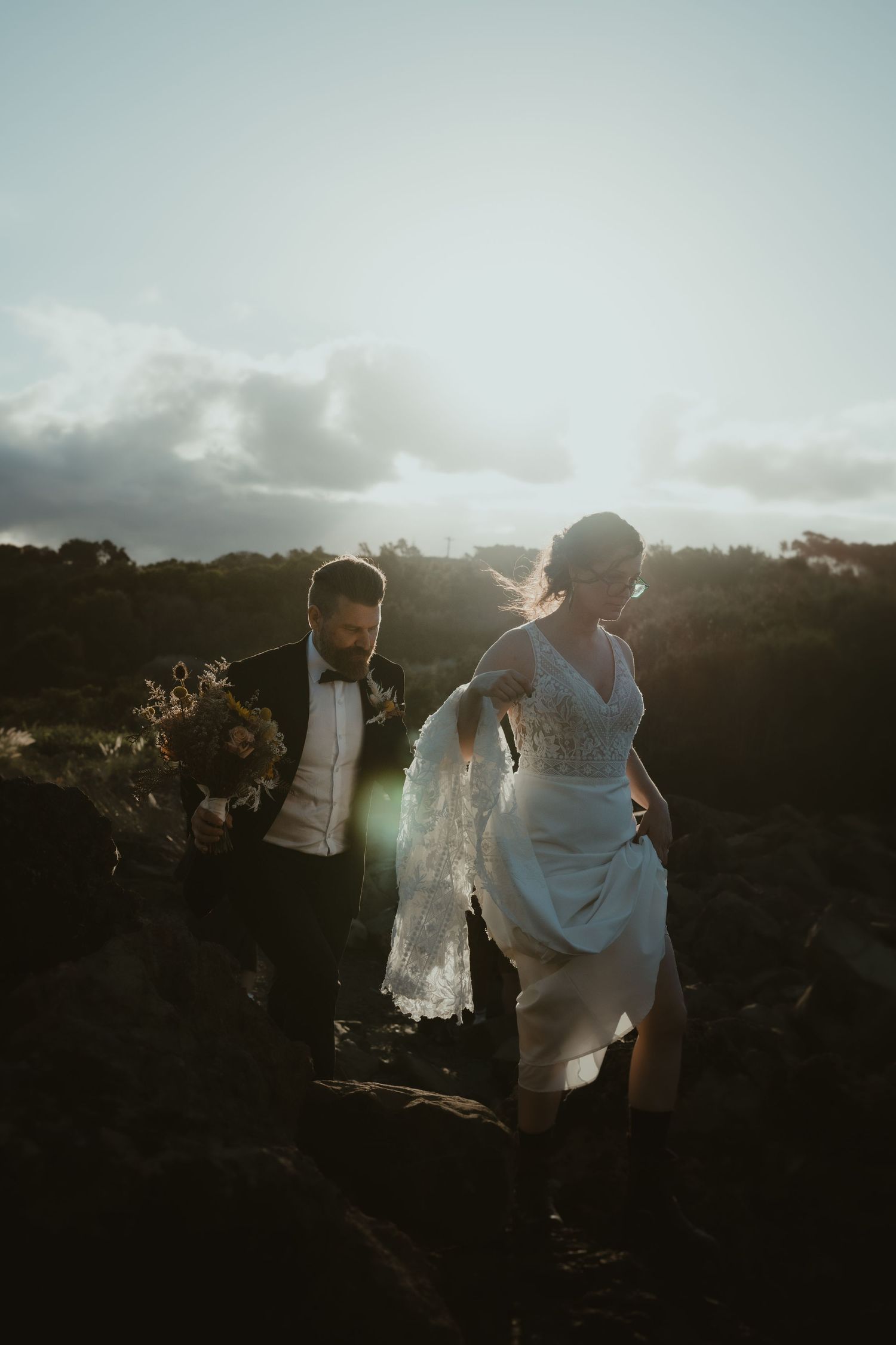 Silhouettes of a wedding party walking along rocky terrain at sunset.