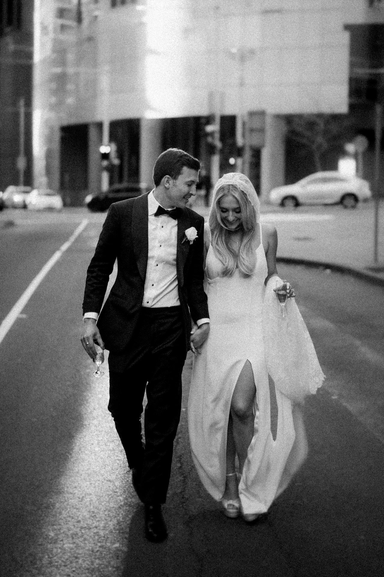 Black and white photo of couple running playfully down an urban street after their wedding.