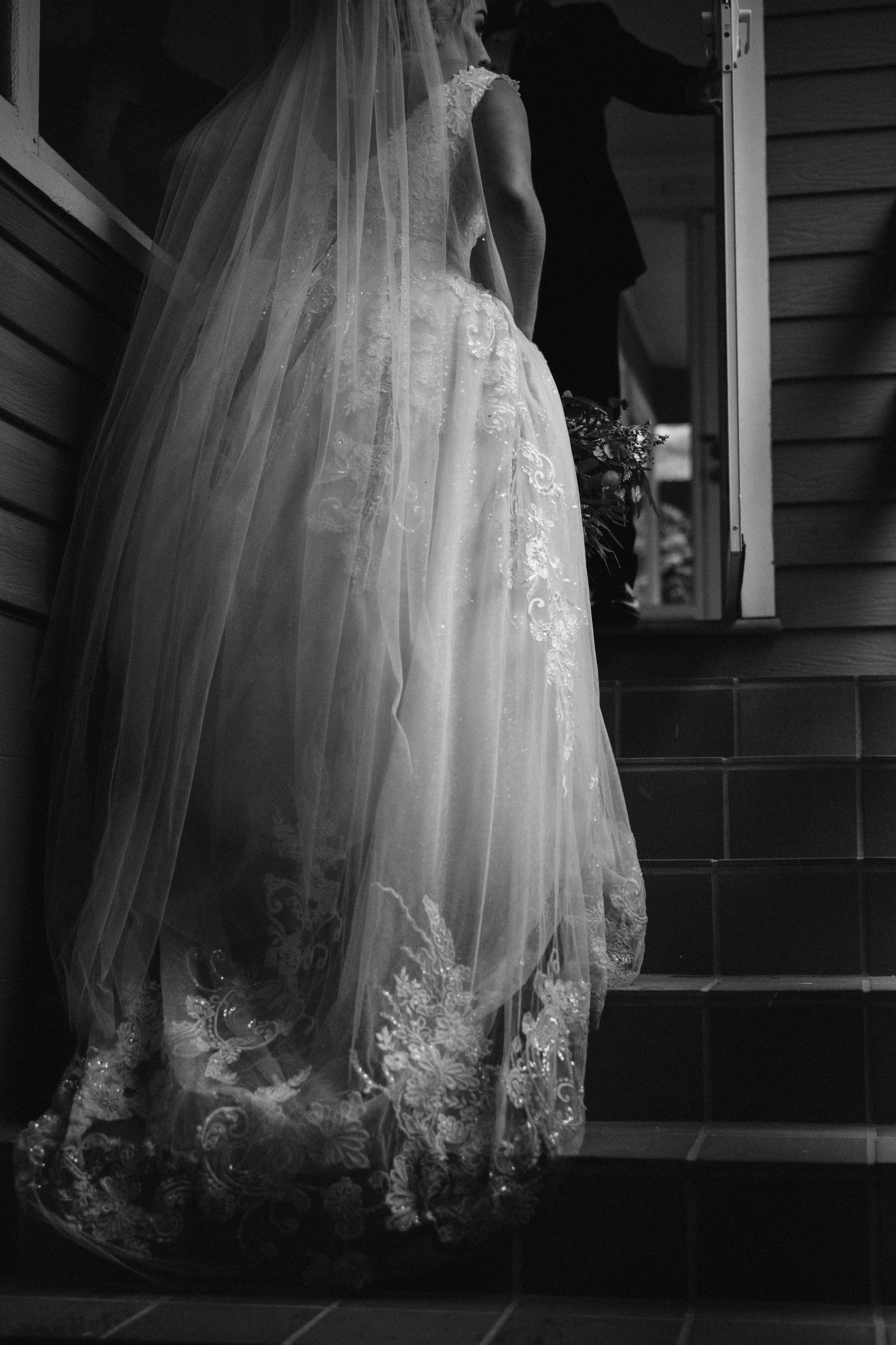 Delicate lace details on a white wedding dress hem create an ethereal silhouette against a dark background.