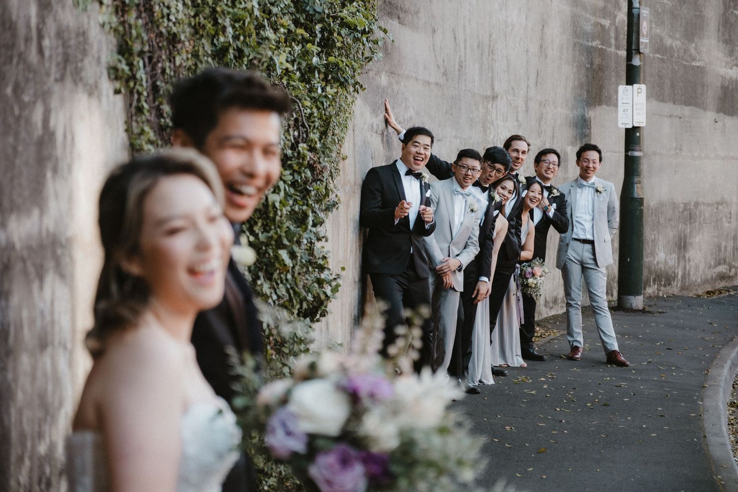 Wedding guests gather outside a stone building adorned with climbing vines.