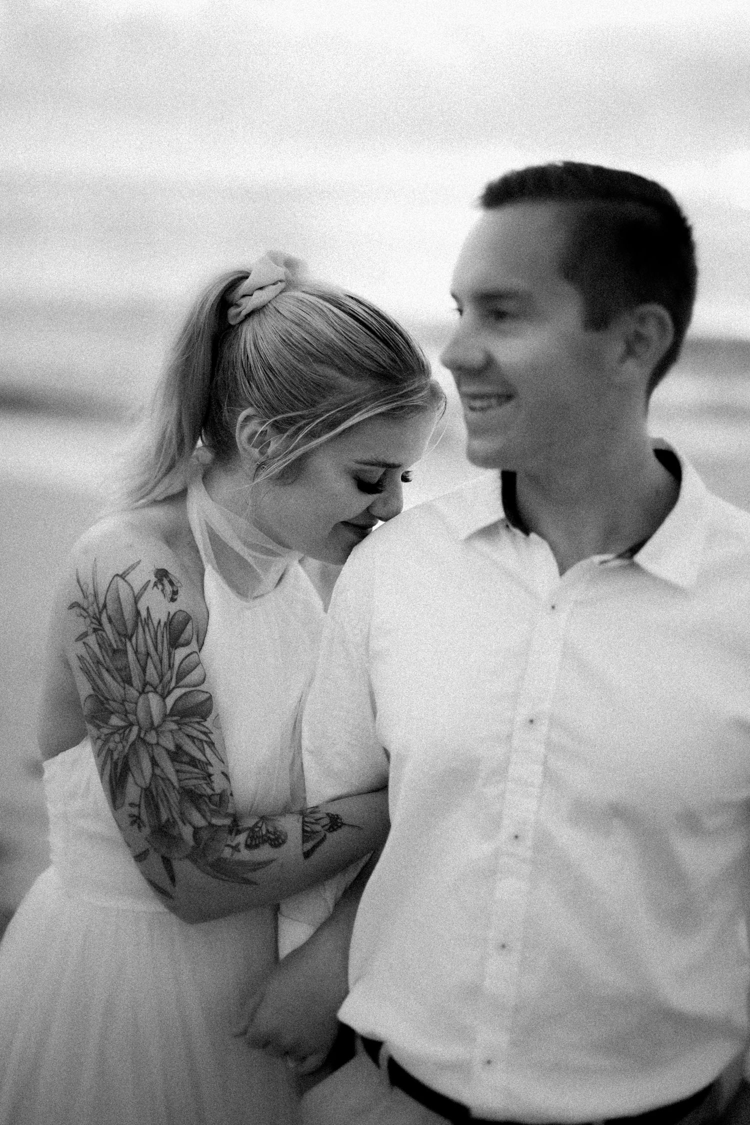 Black and white romantic portraits of a couple in casual attire by the ocean.