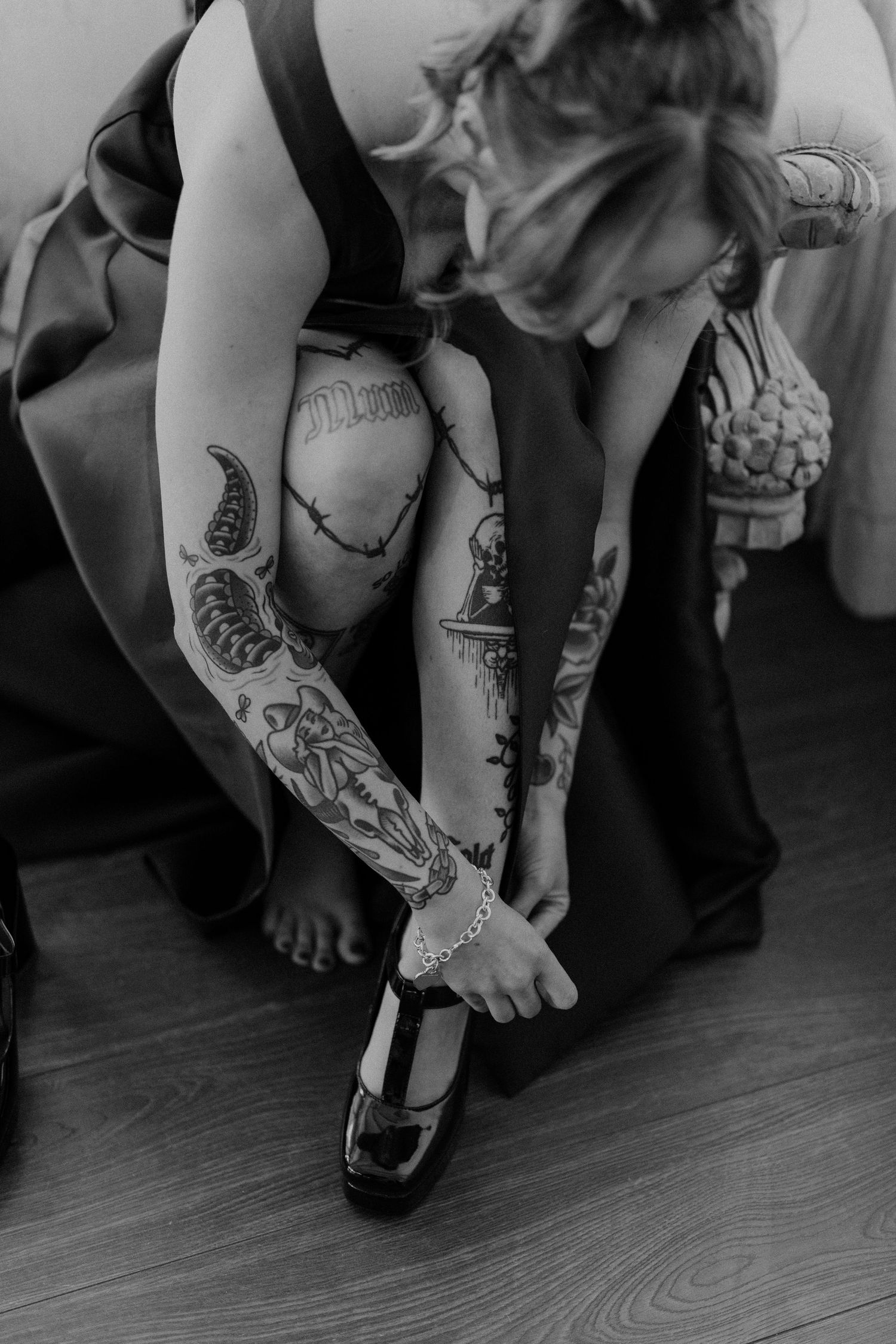 Black and white close-up of tattooed arms showing intricate designs on hardwood floor.
