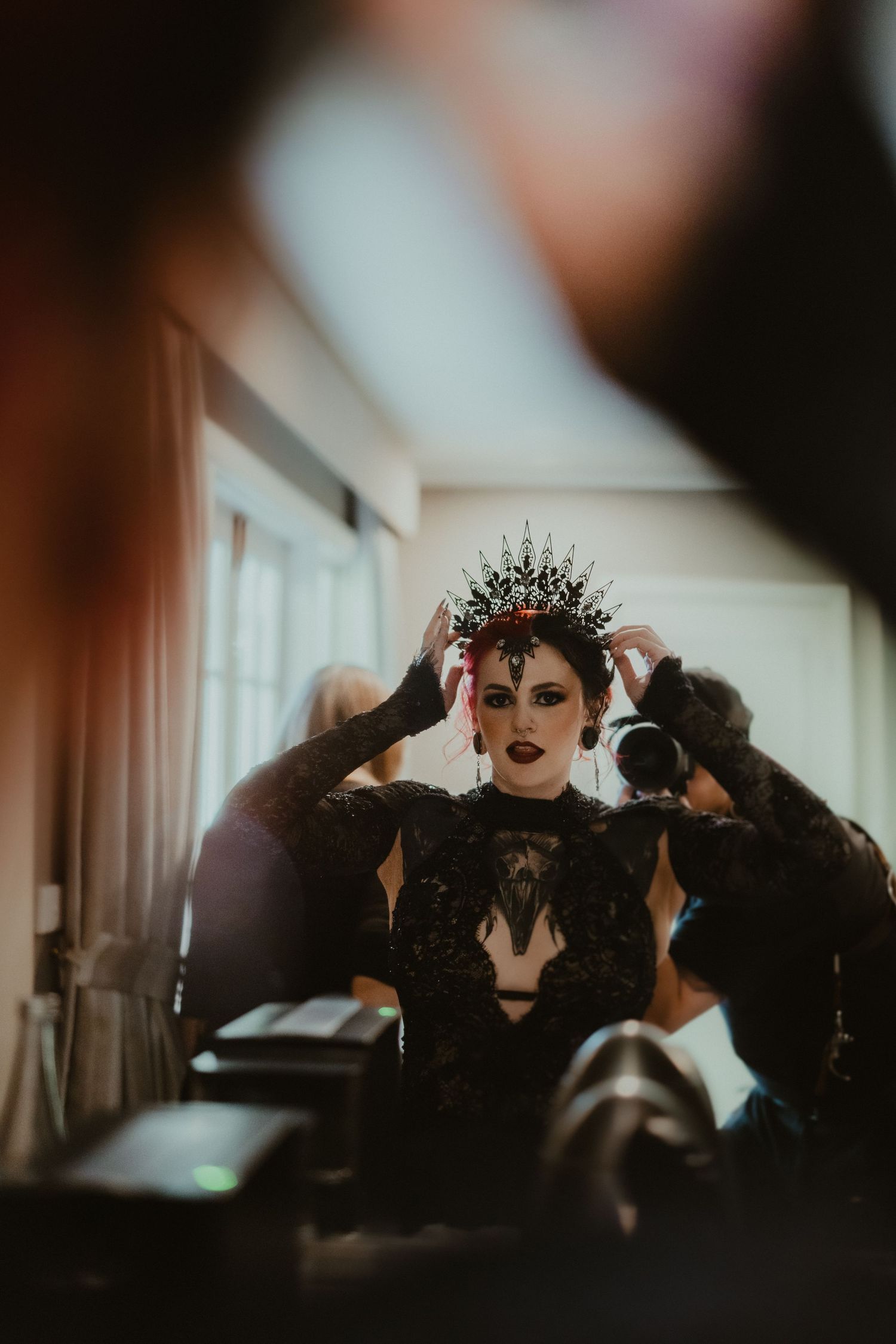 A gothic bride getting ready with a dramatic black crown and dark makeup in moody lighting.