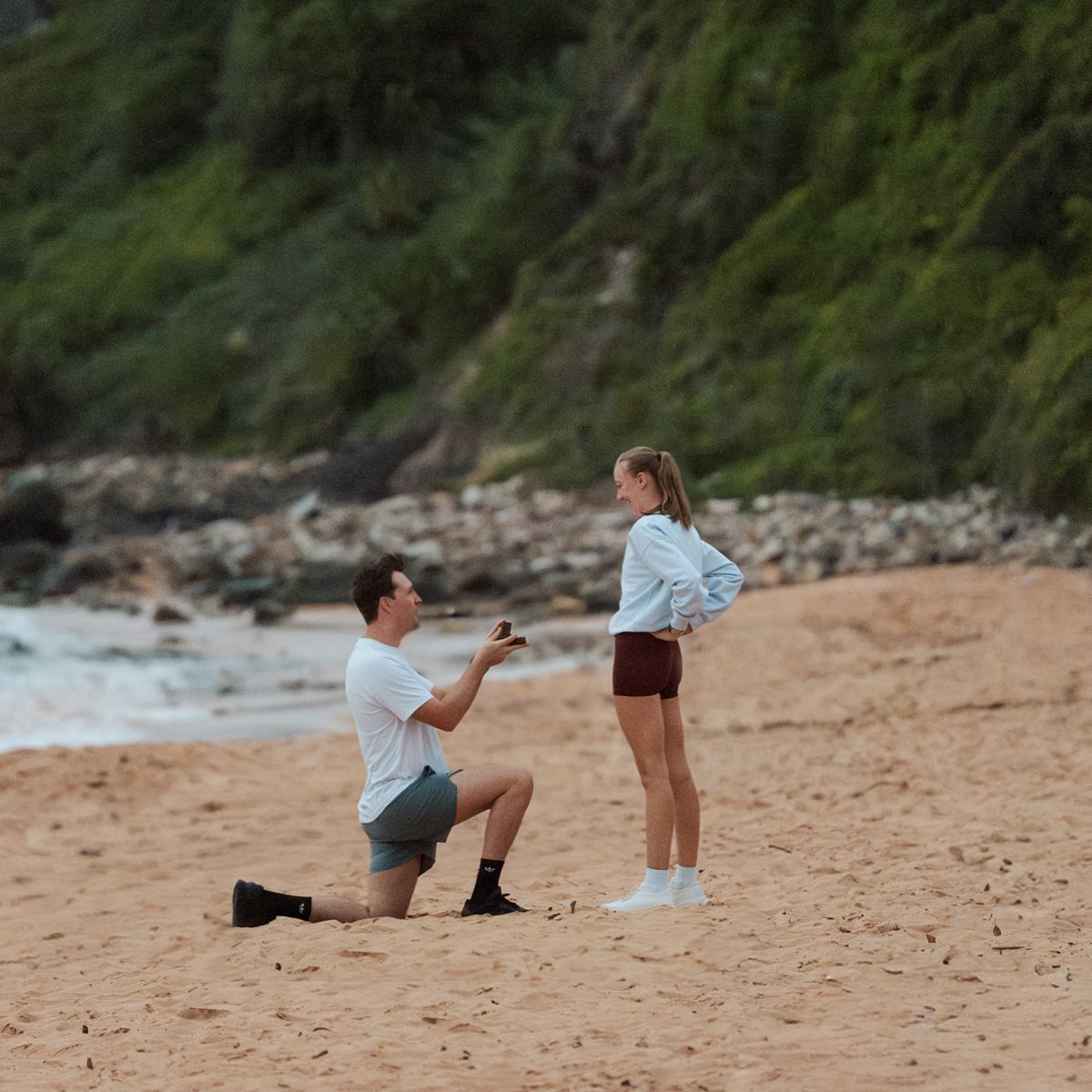 A sequence of photos showing a proposal his girlfriend on a sandy beach with ocean and cliffs in the background in Newport Beach Photoshoot