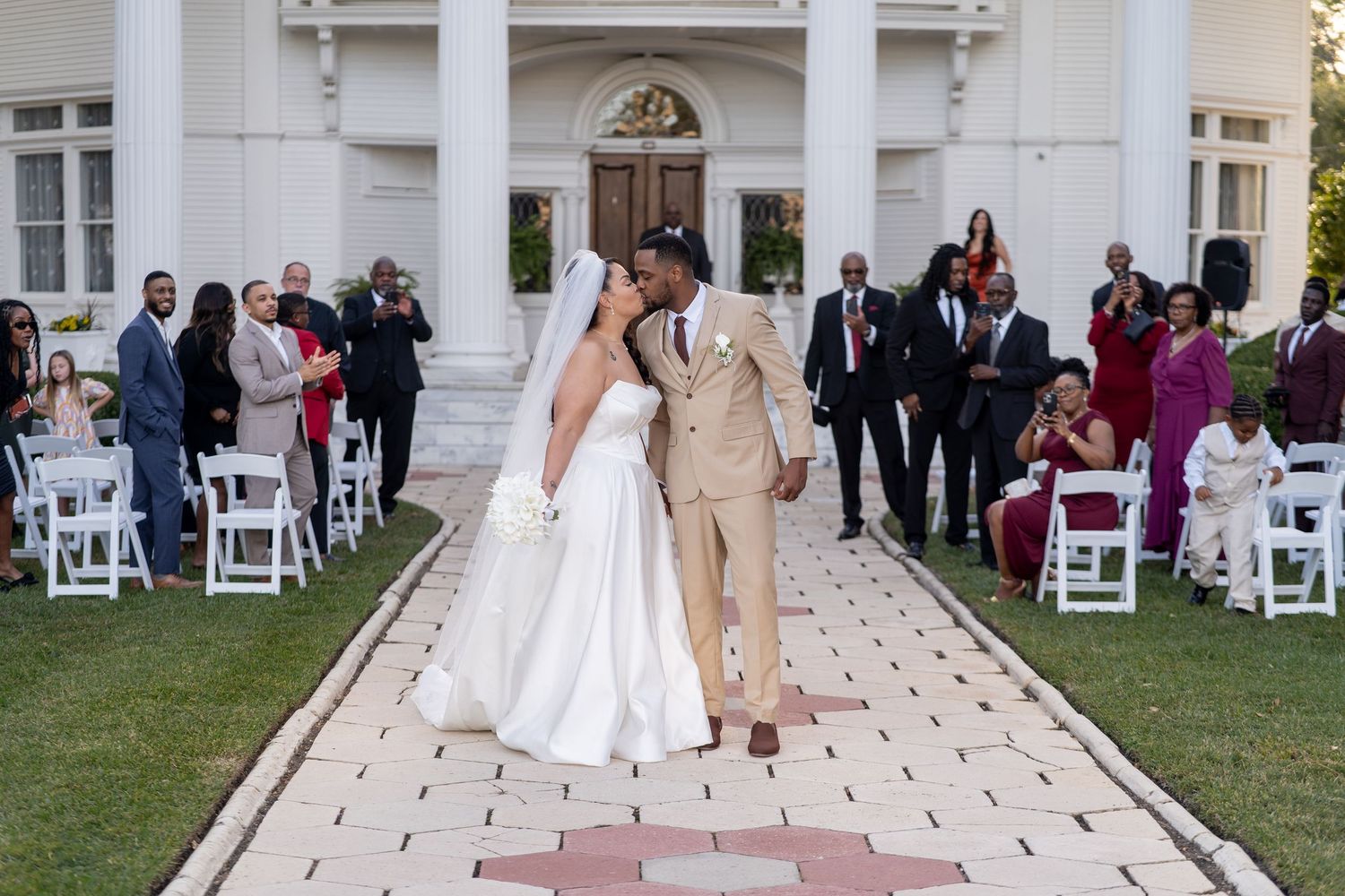 Wedding guests seated in white chairs on a manicured lawn during an elegant outdoor ceremony at a grand venue.