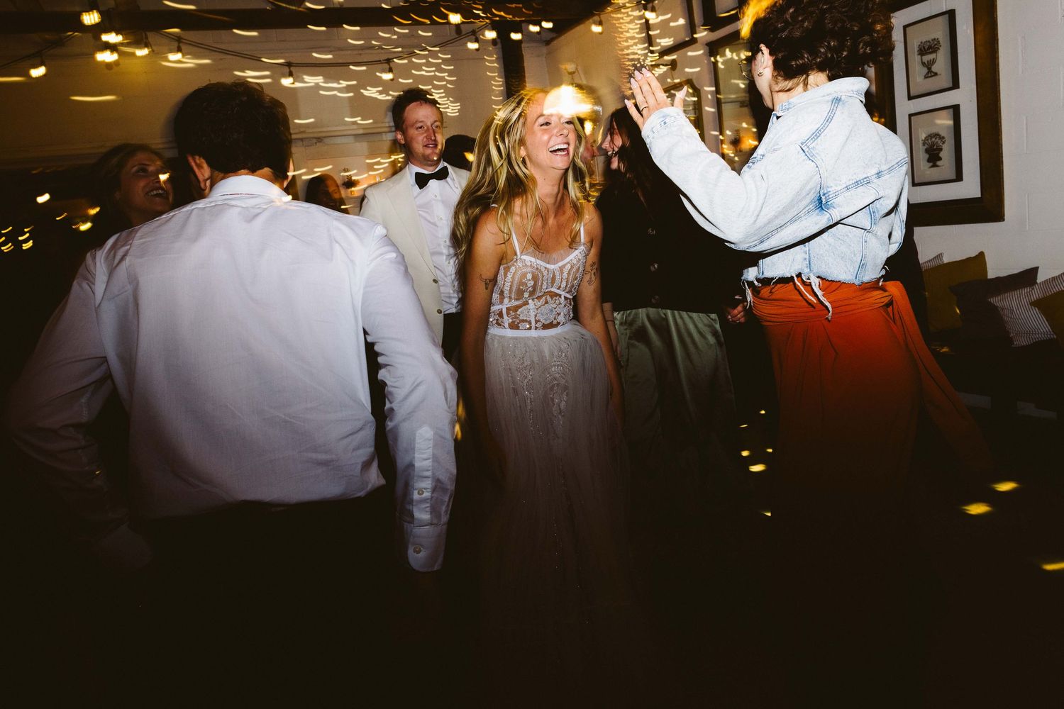 Wedding guests dancing and celebrating on a dimly lit dance floor at an indoor reception venue.