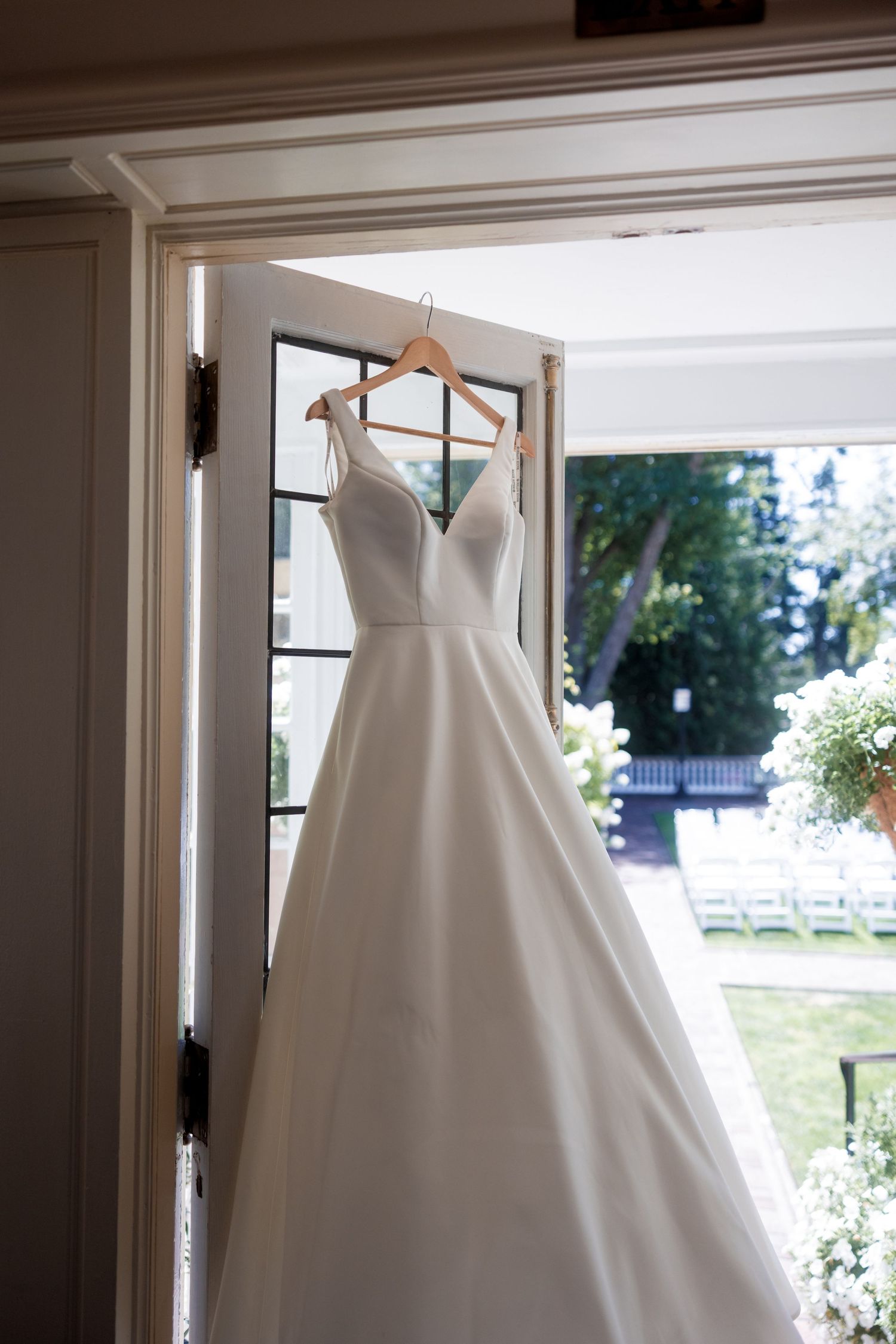 A classic white ballgown wedding dress hangs elegantly in front of a bright window.