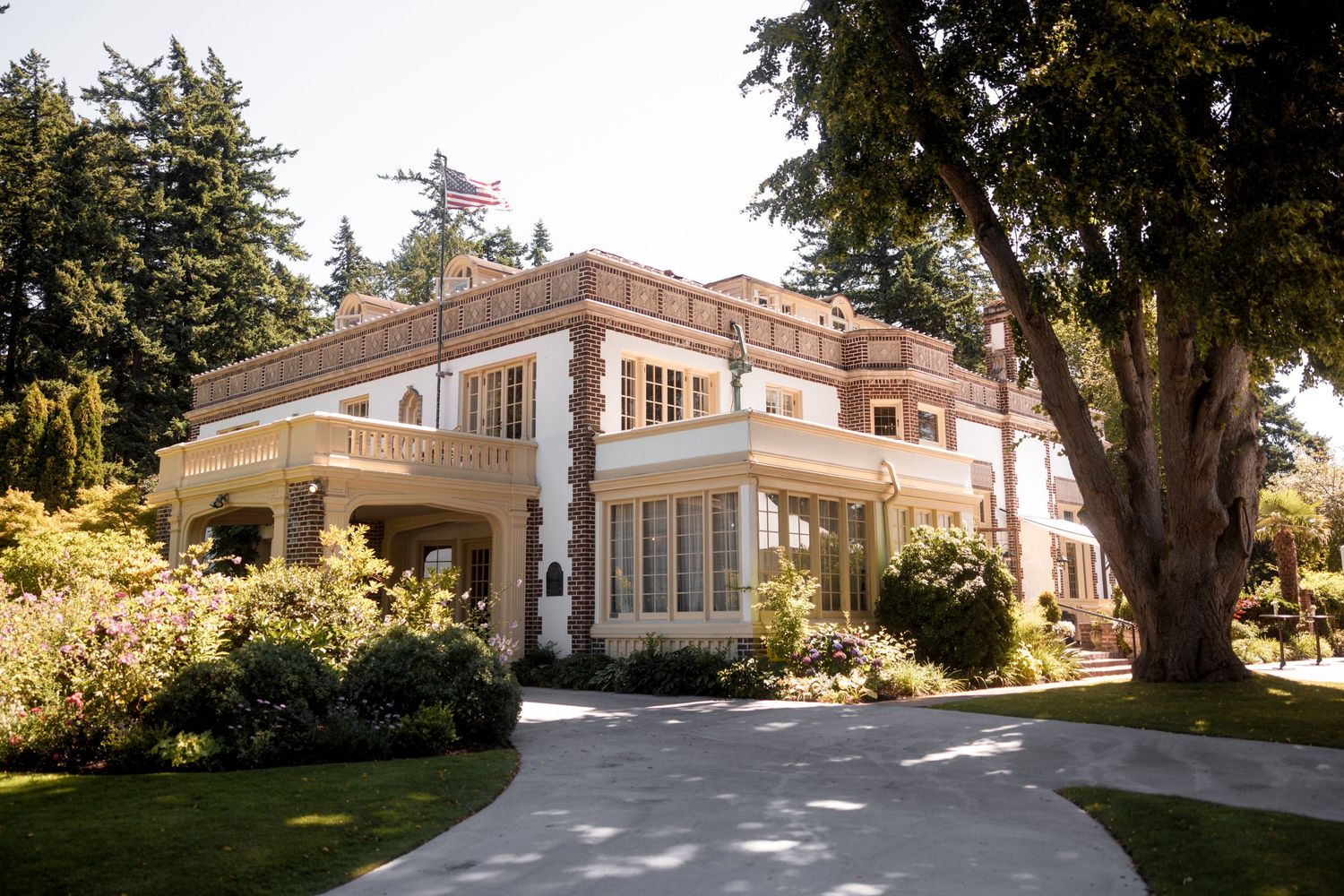 Elegant historic mansion with white columns and curved driveway surrounded by lush gardens and tall trees.