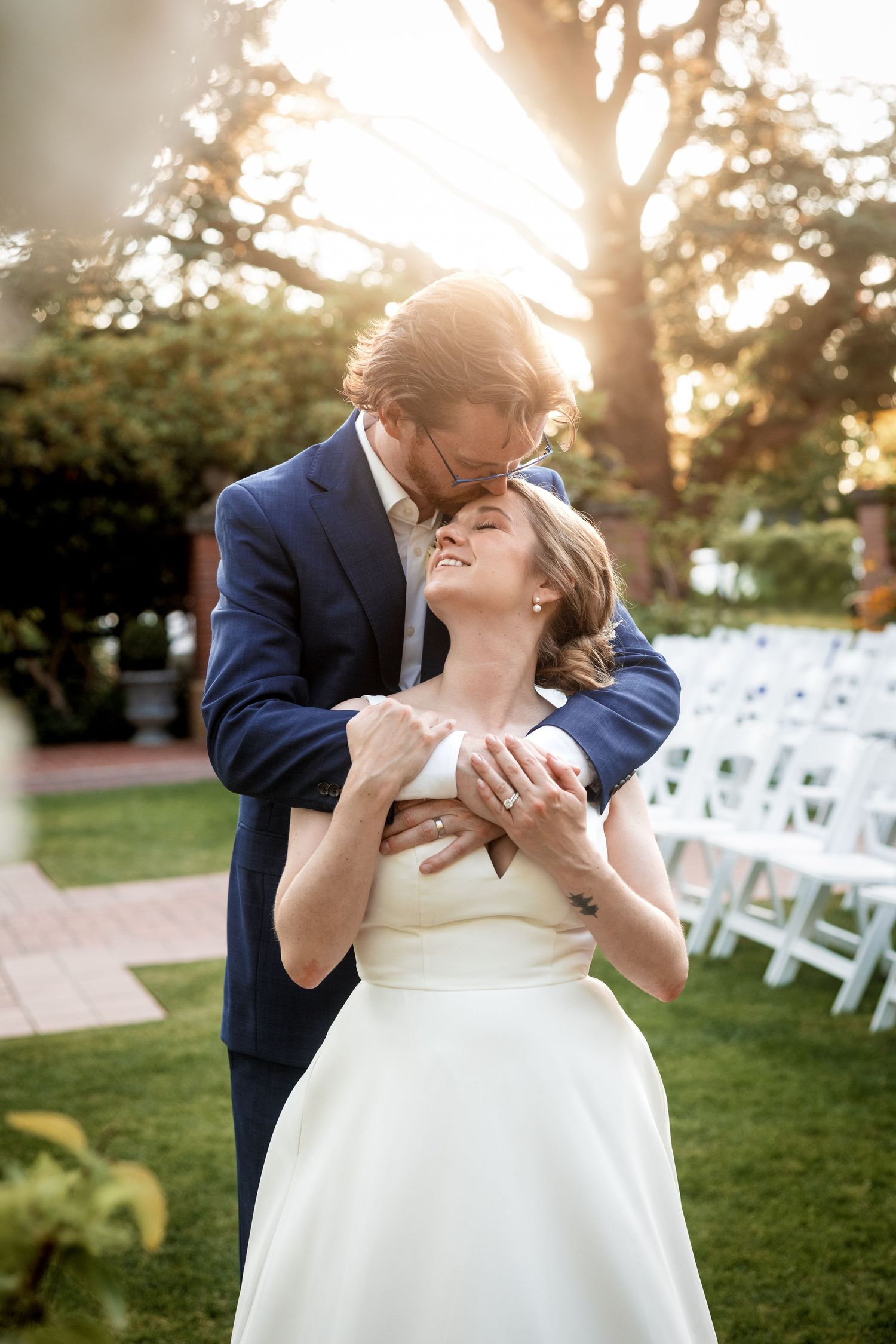 A romantic wedding scene at sunset with white chairs set up on a lawn for an outdoor ceremony.
