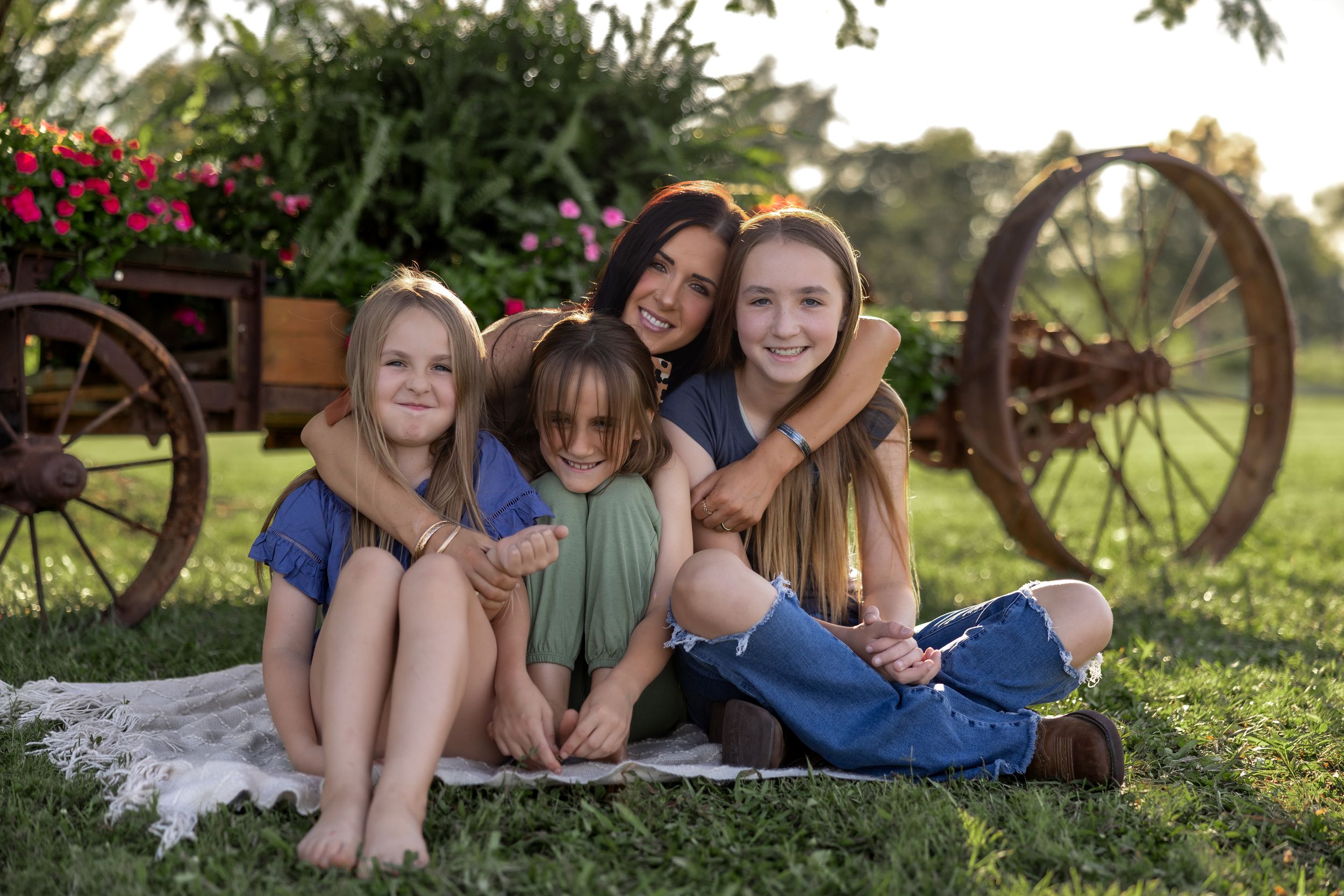 Group photo of friends lying on grass with vintage wagon wheel and flowers in background.