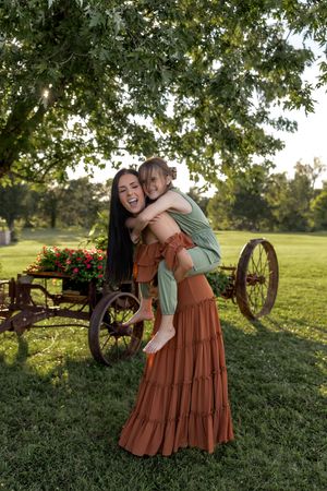 Playful outdoor photoshoot with rustic wagon wheel and blooming flowers in background.