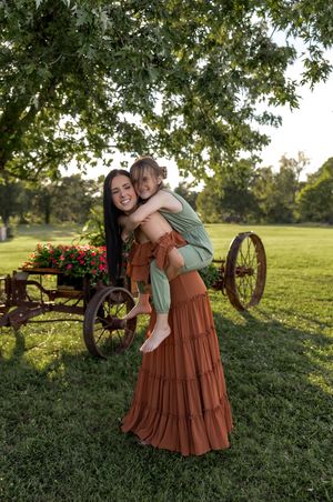 Friends embracing and laughing together near vintage farm equipment in a sunny field.
