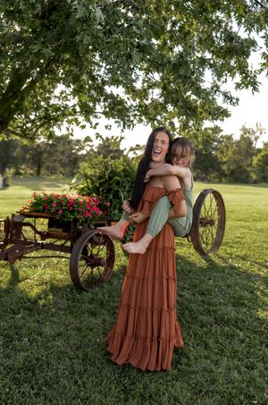 Candid moment of joy captured outdoors with antique wagon and flowering bushes.