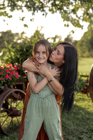 A sweet embrace in a garden setting with blooming red flowers and rustic wagon wheels in the background.