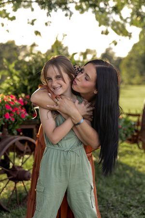 Playful outdoor portrait with an antique wagon and red flowers creating a charming garden backdrop.