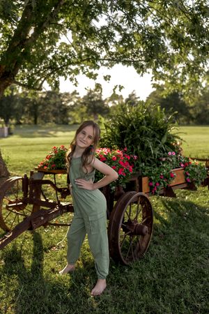 Playful stance by vintage wagon wheel with blooming flowers in late afternoon sunlight.