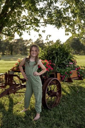 Cheerful garden portrait with vintage wagon wheels and blooming flowers in golden hour light.