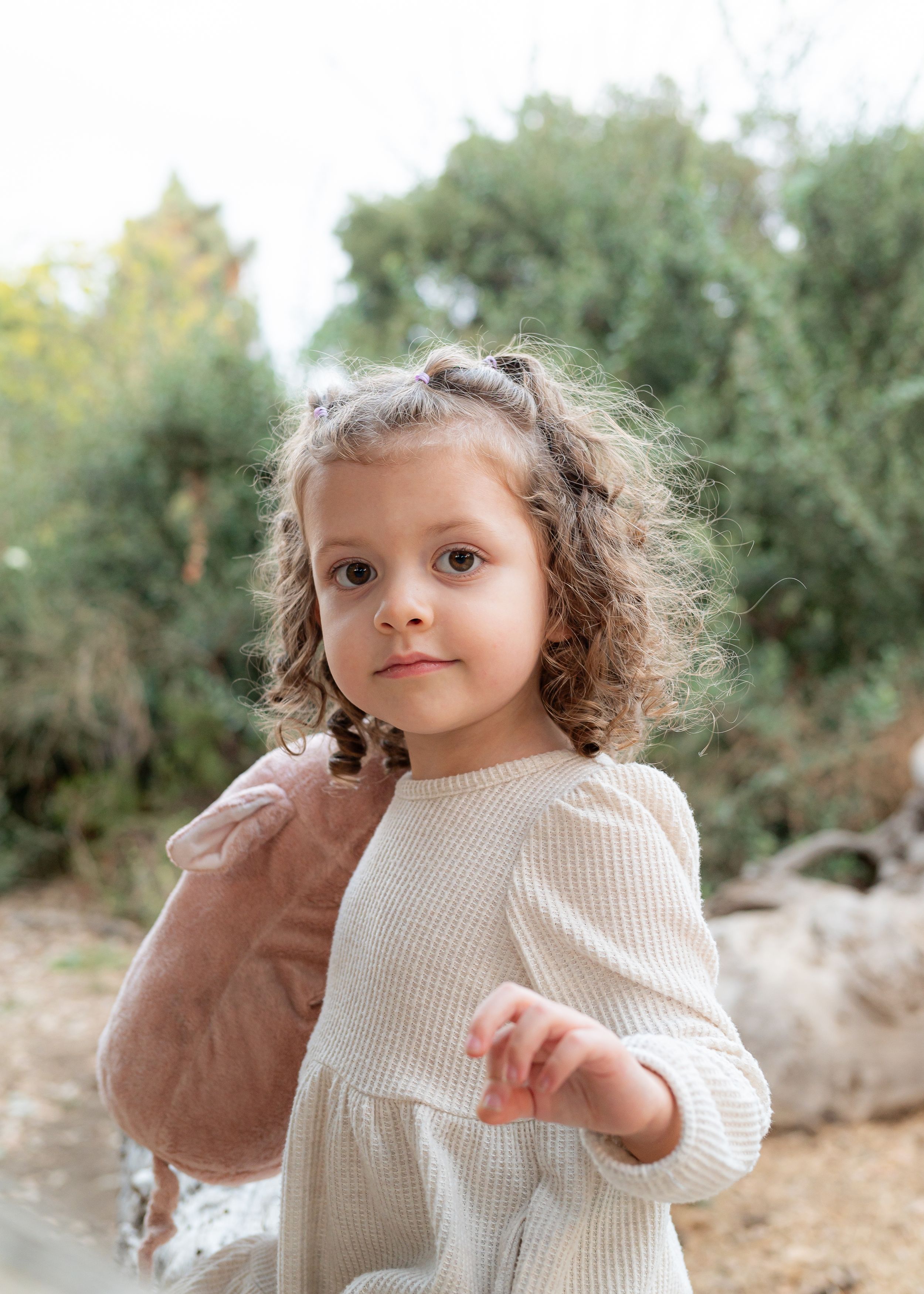 Young child in cream colored dress standing in a desert garden setting.