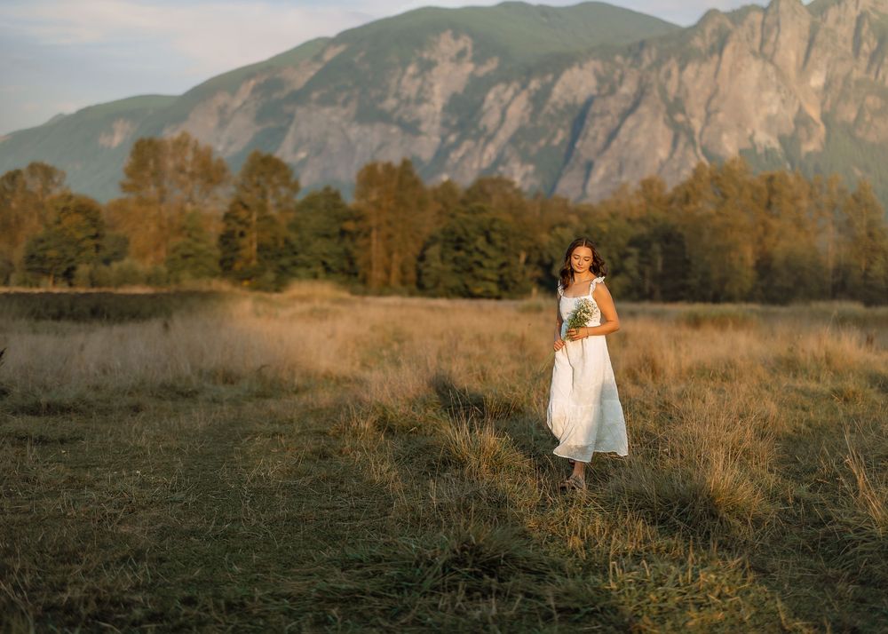 Mountain landscape with figure in white dress walking through golden field.