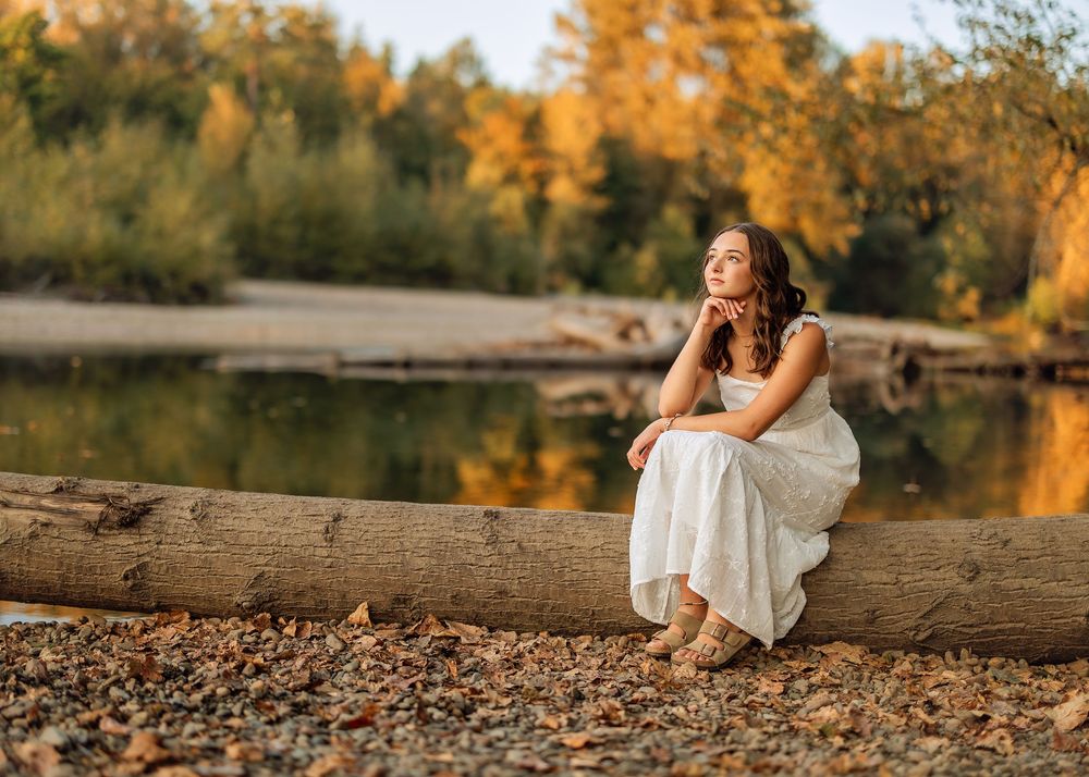 A scenic autumn photoshoot by a rocky riverbank with golden trees reflecting in the water during sunset.