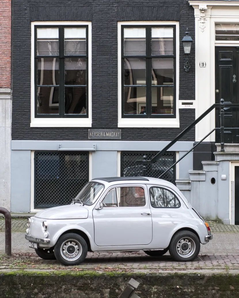 Vintage white car parked in front of a stylish black-and-white townhouse on a quiet street.