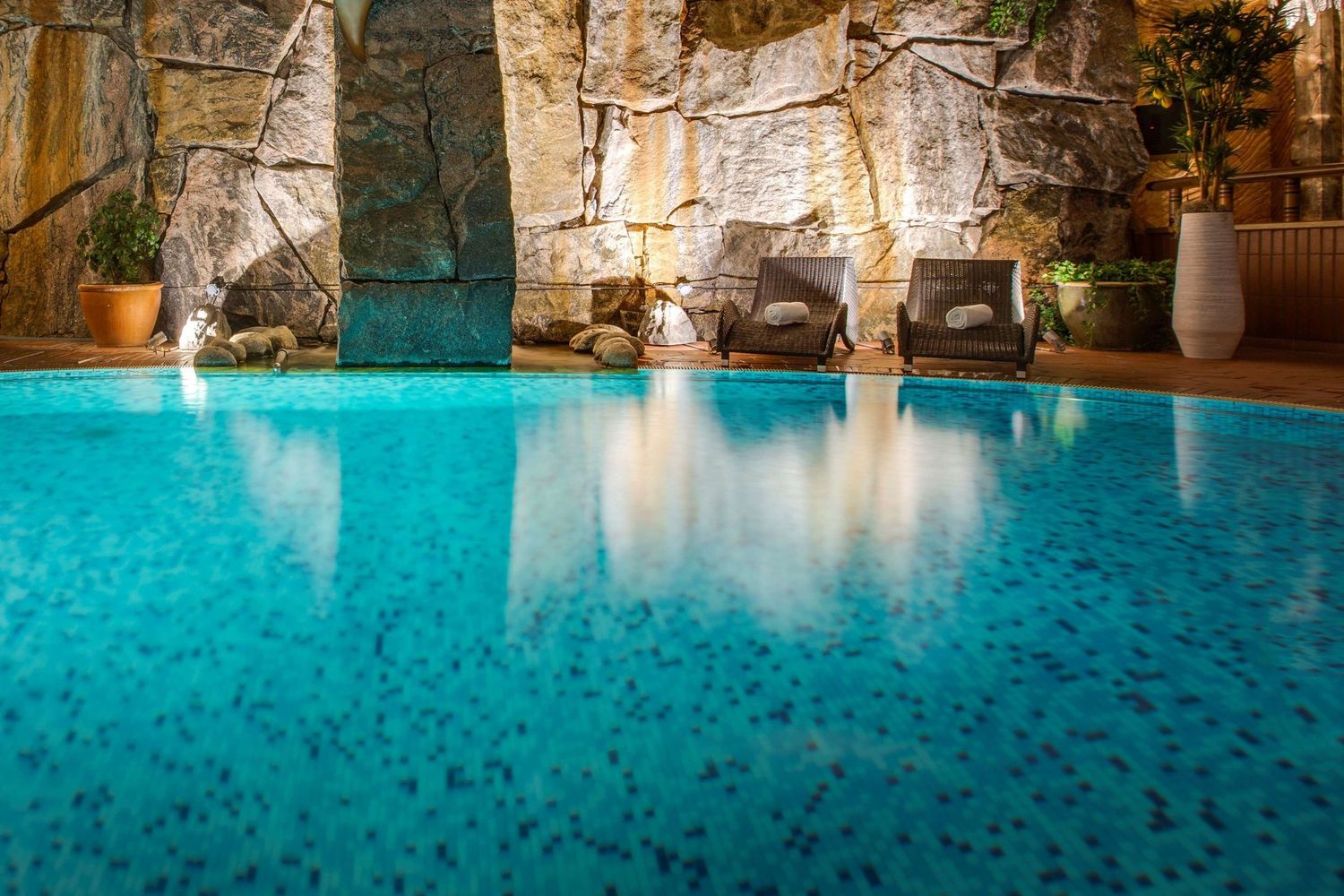 A luxurious indoor pool with turquoise water surrounded by stone walls and archways in a spa setting.