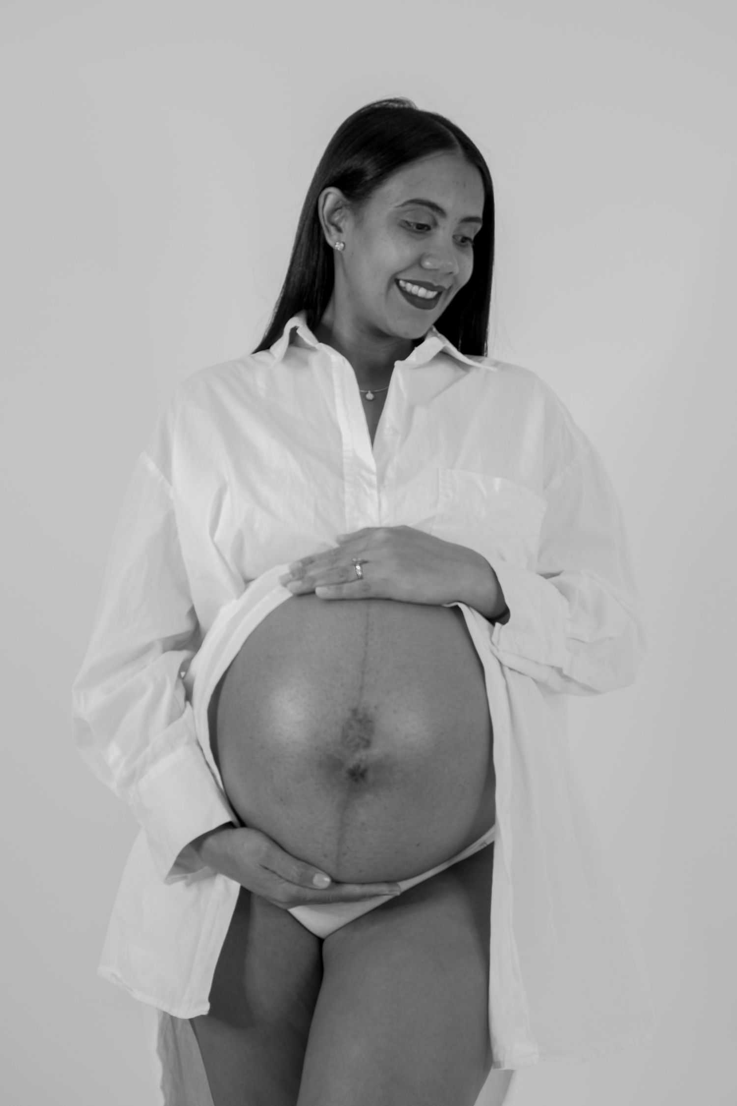 A series of black and white maternity photos showing a pregnant belly in a white button-down shirt.