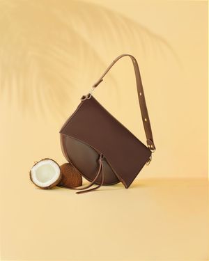 Brown half-moon handbag styled with coconuts and palm shadows, tropical product photography by BOAfoto Vitoria-Gasteiz, Spain, Europe