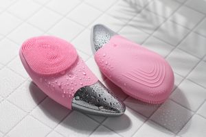 Two pink silicone facial cleansing brushes with metallic tips on wet tiled surface skincare product photography by a professional photograph