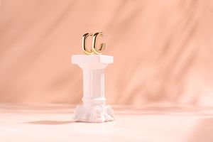 Pendientes dorados tipo aro sobre pedestal blanco de estilo clásico, fondo melocotón y estética cálida, fotografía de producto en Madrid