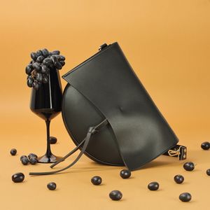 Black designer handbag with gold clasp styled alongside wine glass and grapes, vibrant orange backdrop fashion product photography Spain