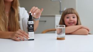 Persona con gotero junto a vaso de agua y suplemento, con niño al fondo fotografía de producto, modelo niña, fotógrafo de productos España