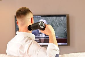 Modell nutzt Massagepistole am Nacken beim Fernsehen — moderne Wellness-Technologie für Entspannung zu Hause, Deutschland