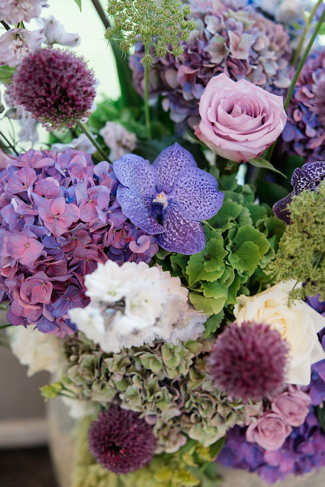 Close-up view of a romantic floral arrangement featuring purple, pink and white blooms with delicate vanda orchids and roses.