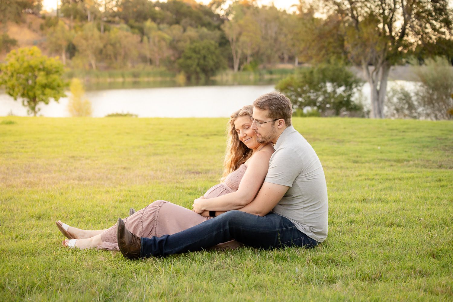A Bay Area couple lounges together on a grassy lawn at sunset during golden hour maternity photo session.