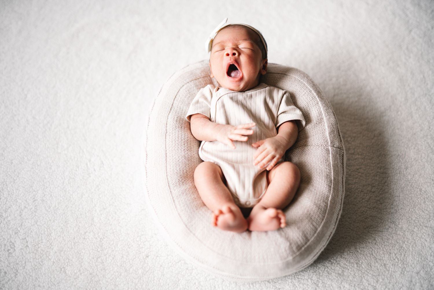 Newborn baby yawning and lying in round cushion during a in-home professional Melbourne newborn photo session.