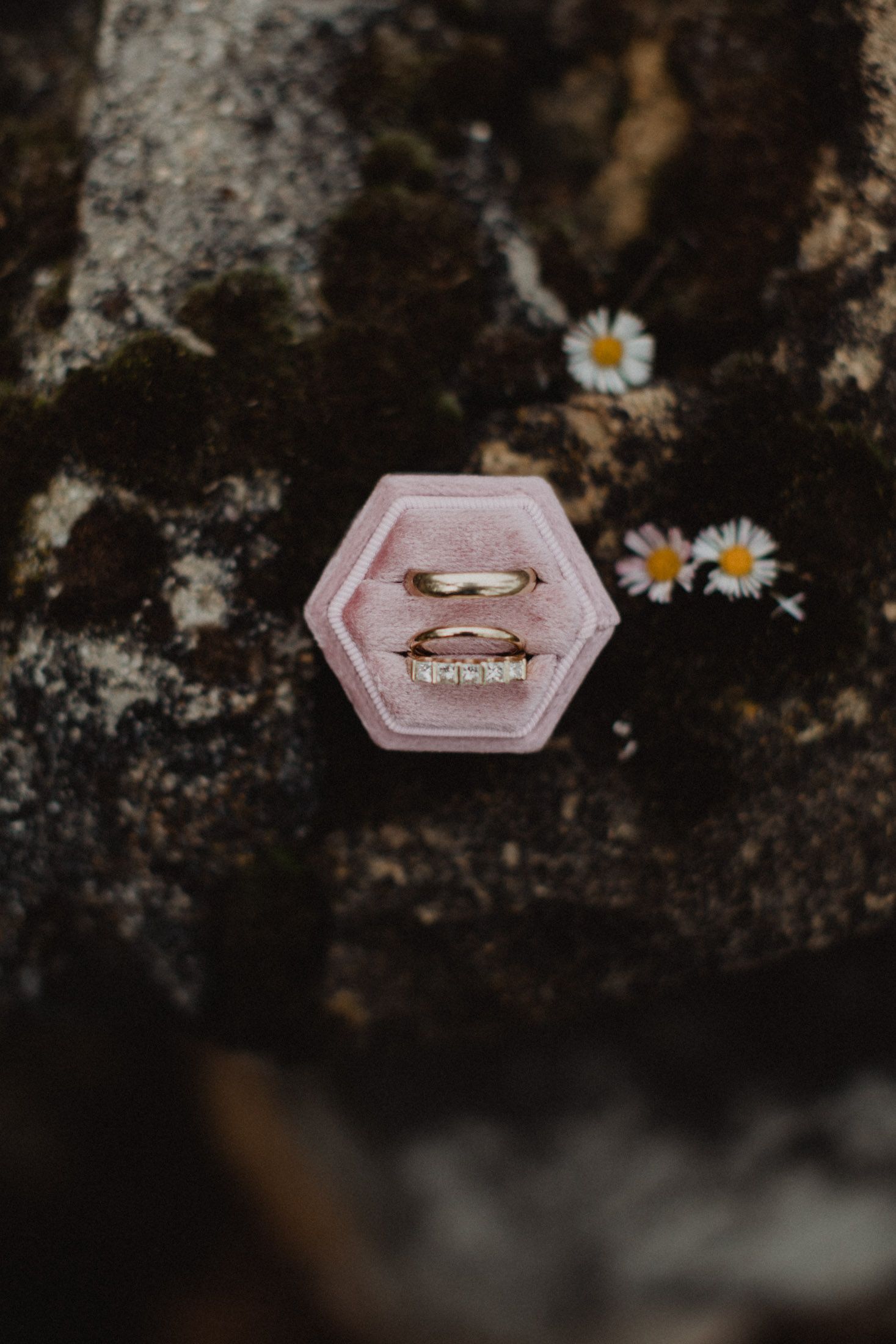 Pink hexagonal ring box with small daisies and sparkly details on a textured dark surface.