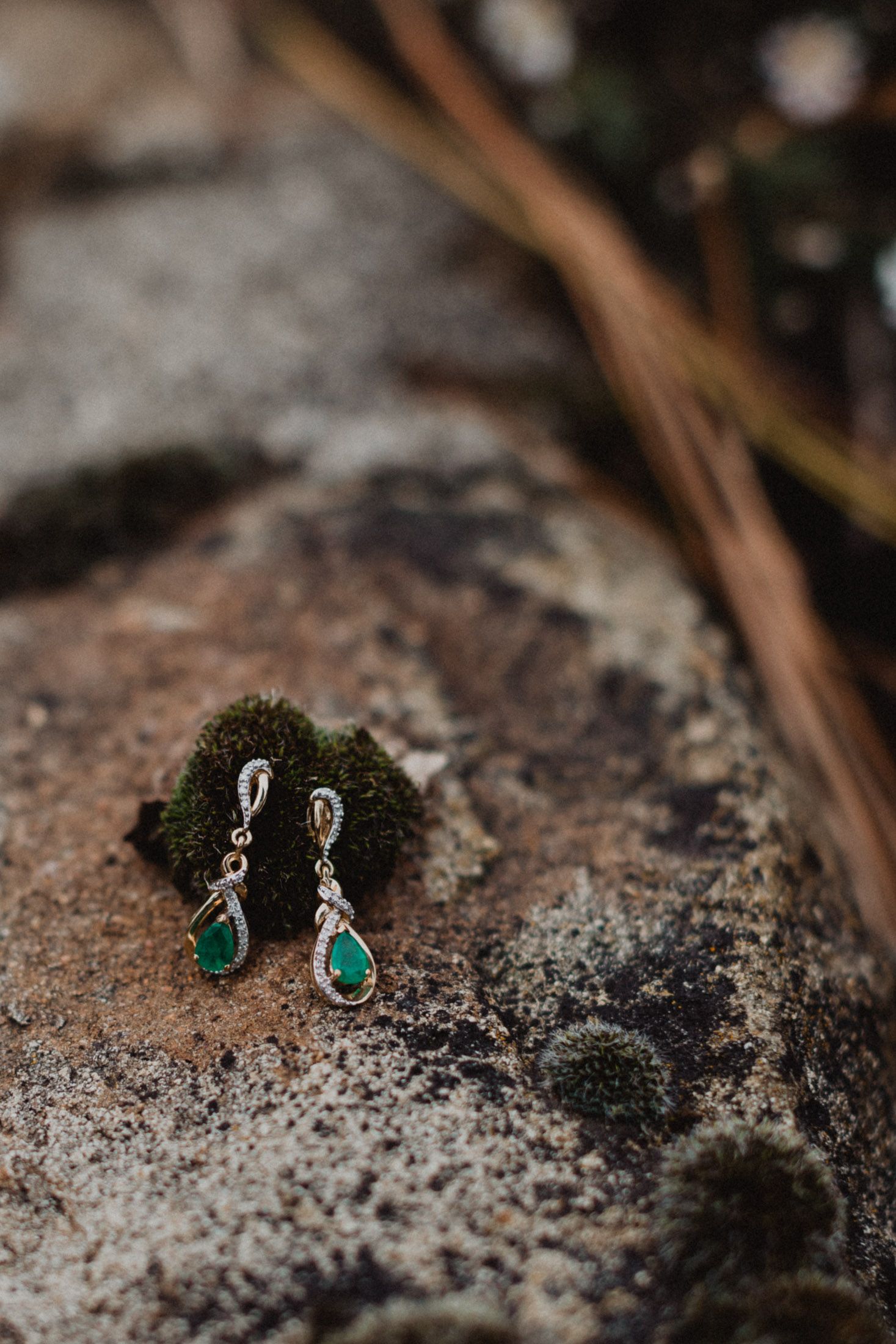 Elegant emerald drop earrings with silver accents photographed on a rustic stone surface.