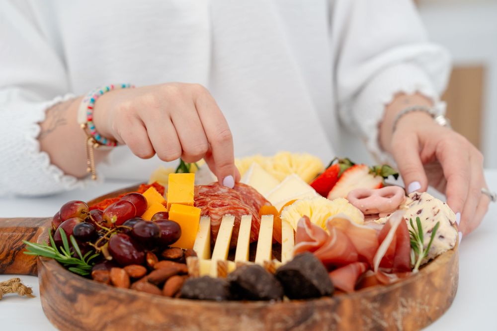 Hands carefully arranging meats and cheeses on a rustic wooden serving board.