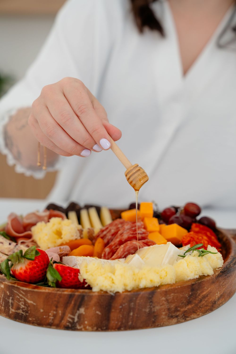 Close-up view of hands arranging meats, cheeses and fruits on a rustic wooden charcuterie board.