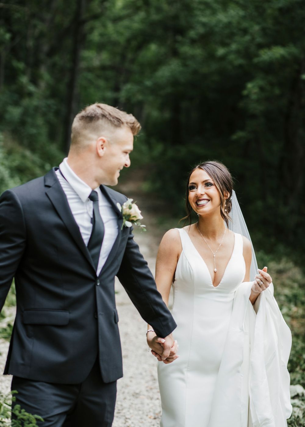 Elegant wedding couple shares intimate moments while walking along a forest trail.
