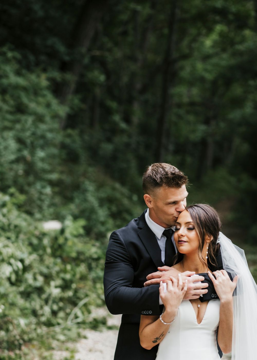 Romantic wedding portraits captured in a lush forest setting with natural lighting.