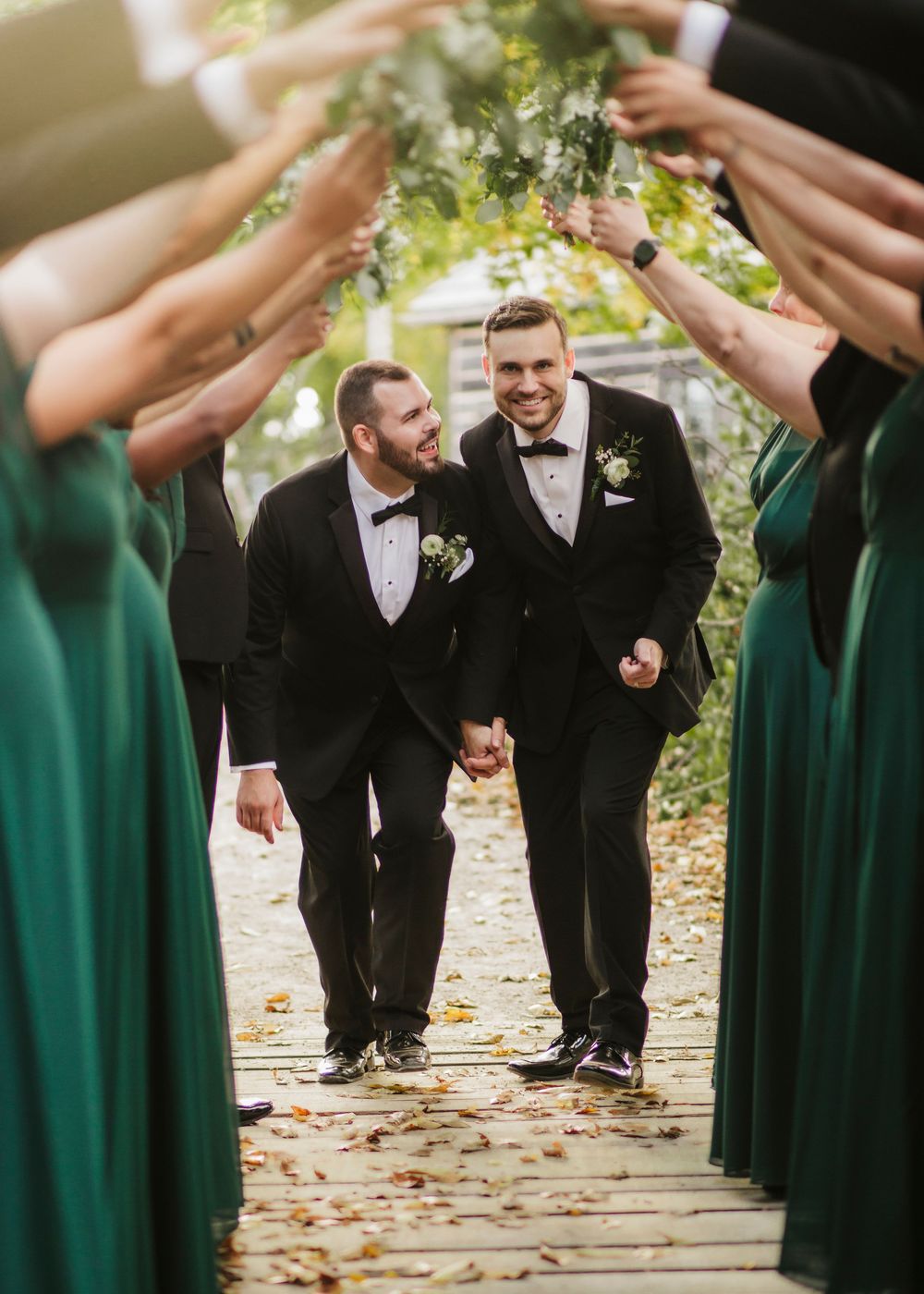 Wedding party creates a tunnel effect with bridesmaids in emerald dresses and groomsmen walking through.