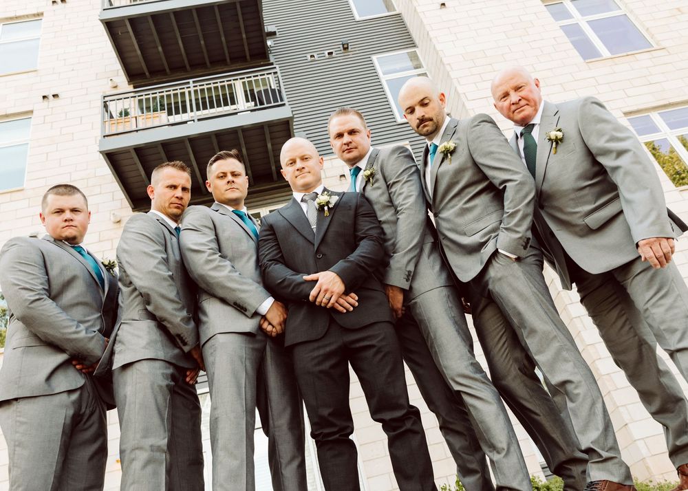 Groomsmen posing casually in gray suits against modern building exterior.