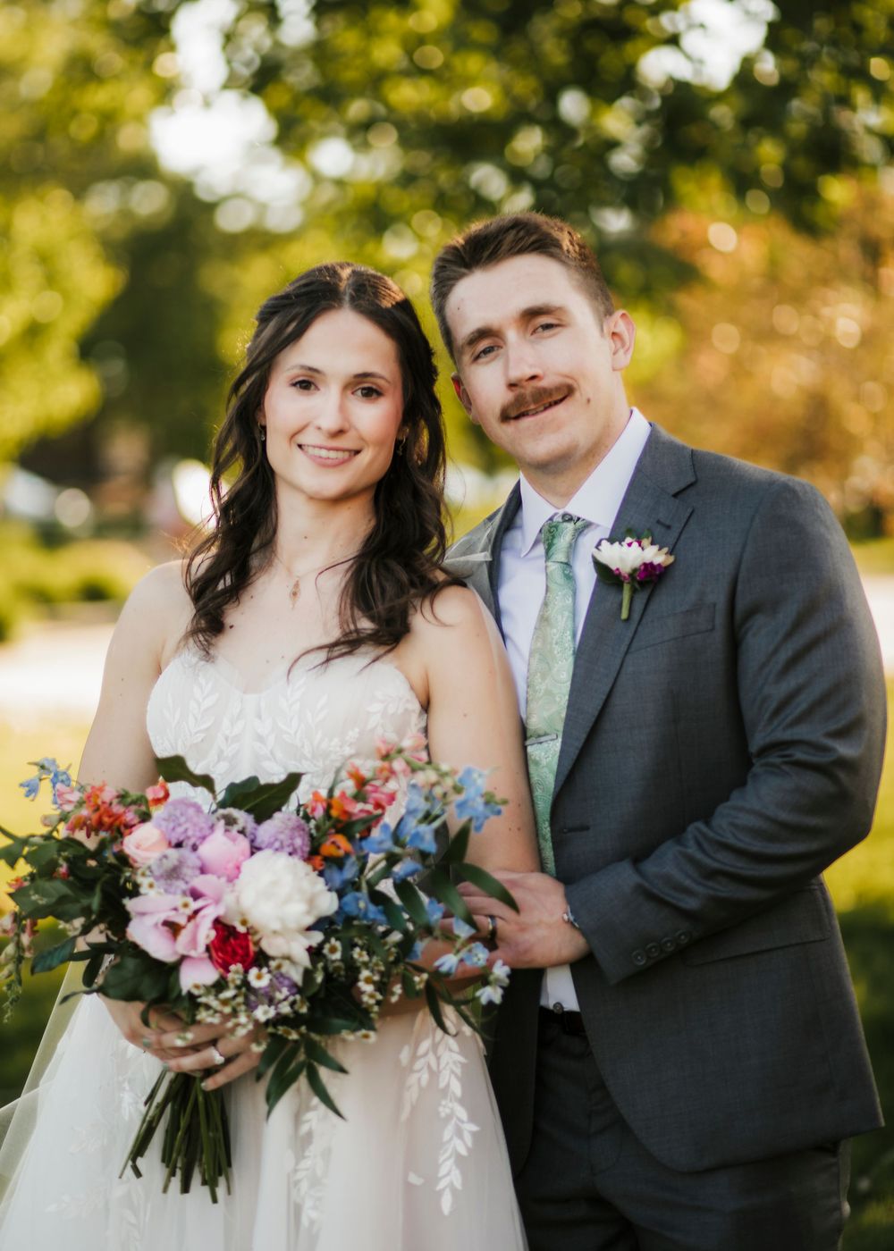 Couple poses outdoors with vibrant autumn wedding bouquet featuring colorful flowers.